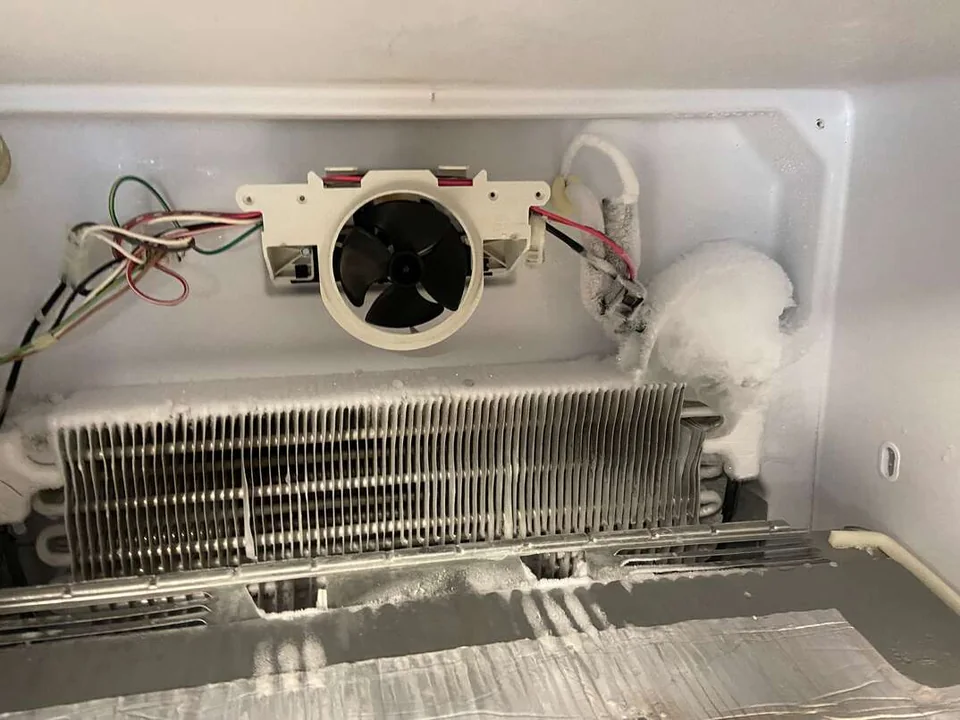 Fridge freezer compartment opened with frosted evaporator fins and the fan motor
