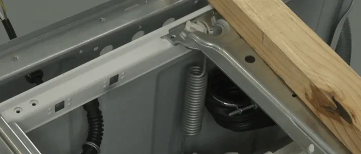 Inside a washing machine cabinet showing the suspension spring and water inlet valve area